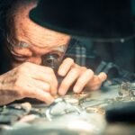 A skilled senior watchmaker examines wristwatches using a loupe under focused lighting.