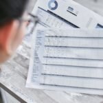 A businesswoman reviewing financial spreadsheets with charts and graphs in an office setting.