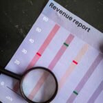 A magnifying glass on a vertical bar chart titled "Revenue report" showing monthly data analysis.
