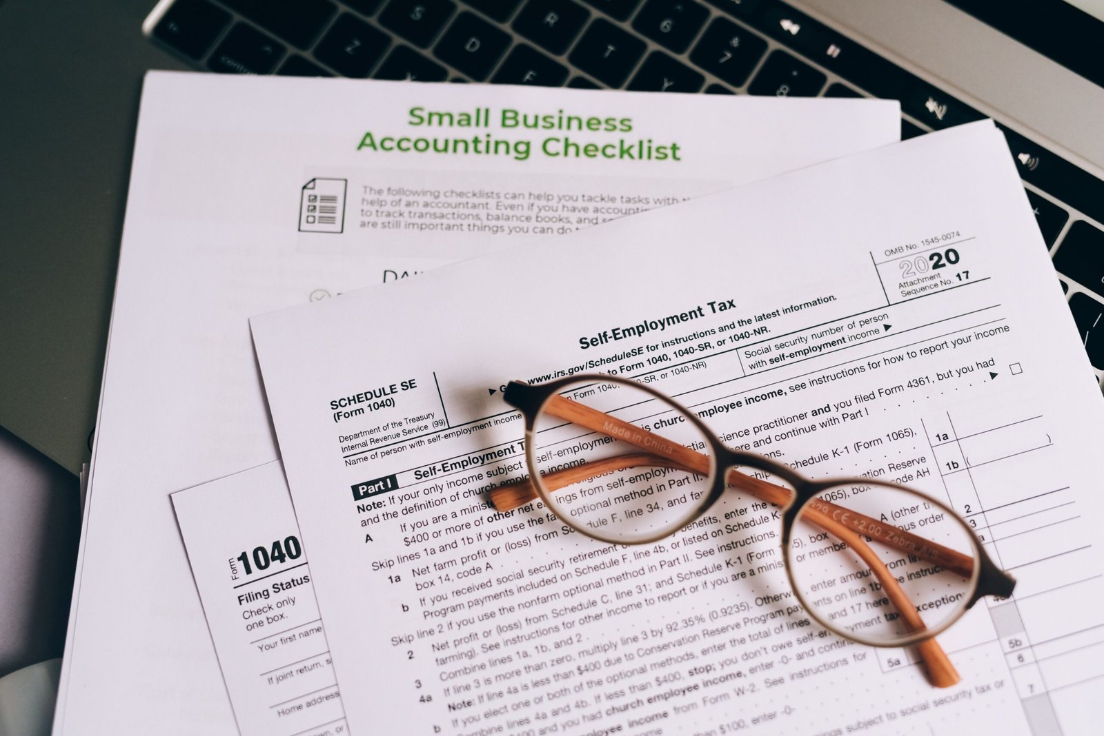Close-up of tax forms and a small business accounting checklist on a laptop.